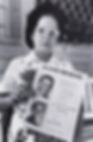 Woman holding a $1,000 reward flyer with two boys' photos. She's wearing glasses and a patterned dress. Porch scene with flowers.