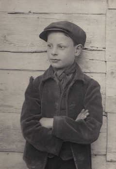 Young boy in flat cap with crossed arms against wooden background.