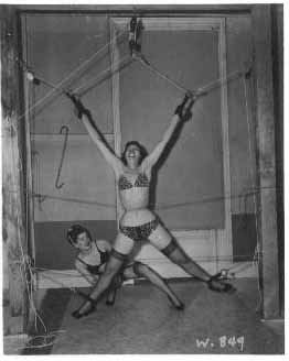 Two women in lingerie, one suspended in X-shape, another below.