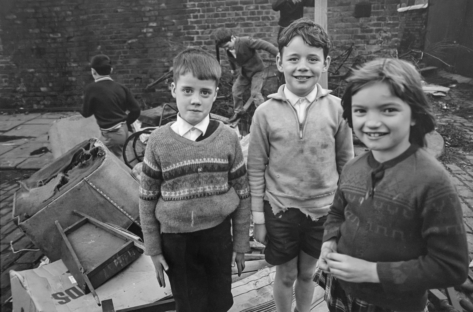 Three smiling children, two boys and a girl, standing outdoors.