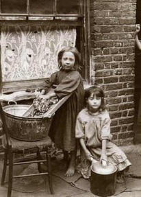 Two young girls, one standing by wash basin, old sepia photograph.