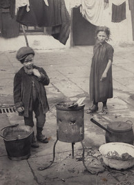 Two impoverished children cook food on a makeshift outdoor stove.