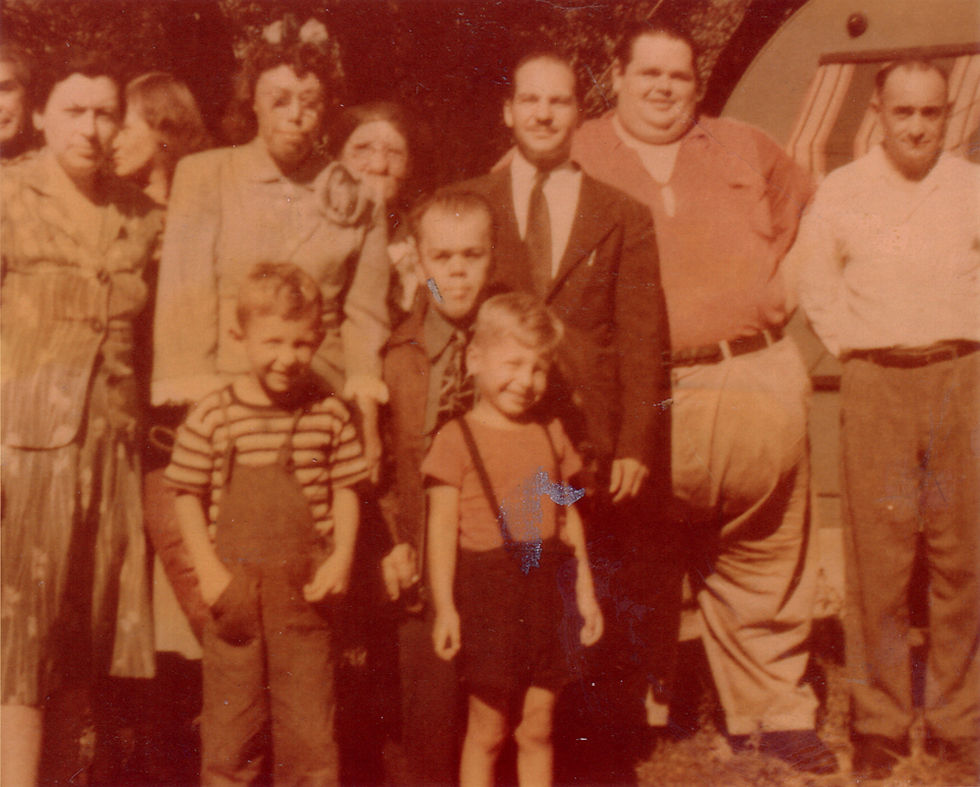 A sepia-toned group photo of ten people, including adults and children, standing outdoors with a trailer in the background. They appear relaxed.