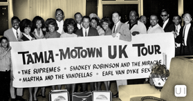 Black-and-white group posing with a Tamla-Motown UK Tour banner listing The Supremes, Smokey Robinson, Martha and the Vandellas.