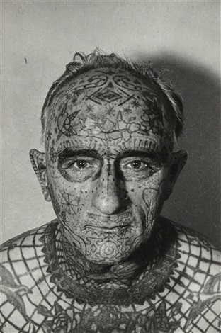 Elderly person with intricate facial and head tattoos looking directly