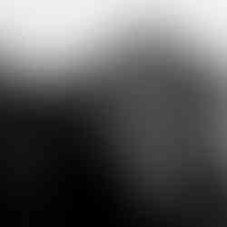 Black-and-white photograph of a Bedouin woman holding a swaddled infant in her arms, standing outside a large traditional tent. The woman wears patterned sleeves and a headscarf, gazing gently at the baby in soft morning or evening light. Taken in the early 20th century by the American Colony Photo Department.