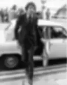 Bum Farto, wearing a dark suit, steps out of vintage car.