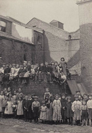 Historical image: many children sitting on brick wall, old urban street.