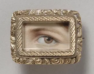 A brown human eye framed in an ornate golden miniature.