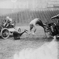 Vintage image of people in early motor cars, one flipping over, another with a mallet. Action scene on a grassy field, chaotic mood.