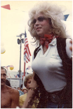 Blonde individual wearing red bandana, white shirt, vest at festive event.