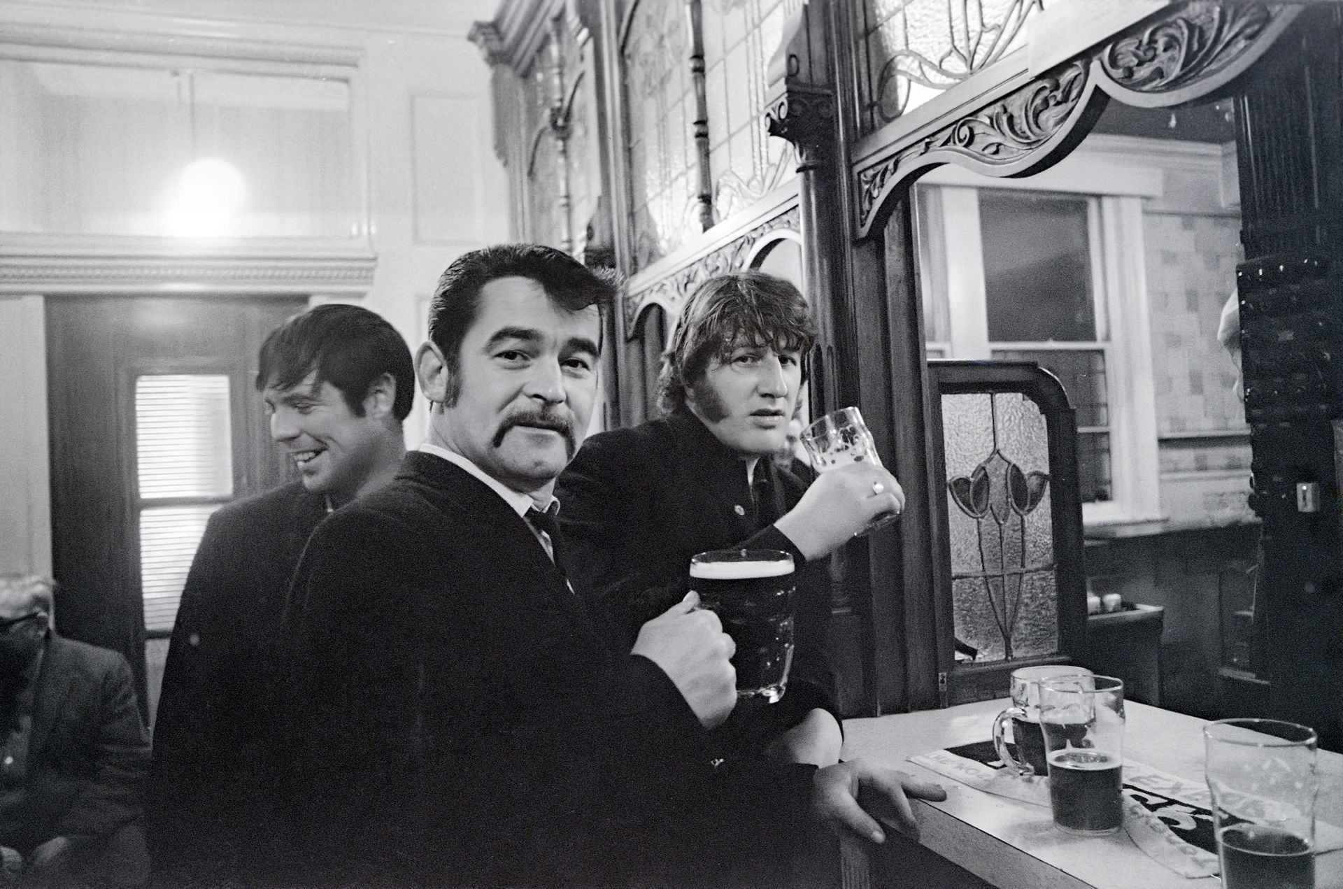 Three men, including John Lennon, drinking in a classic bar.