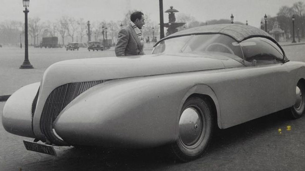 Man admiring sleek vintage car with long hood and covered wheels.