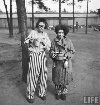 Two women, survivors, hold bowls in striped prison camp attire. LIFE.