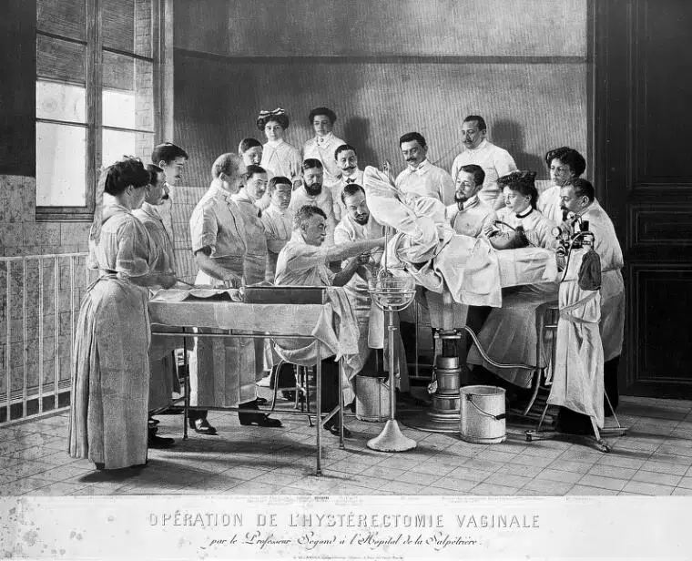 Medical team performs surgery in a vintage operating room with spectators. Doctors in white coats focus intently on the procedure.