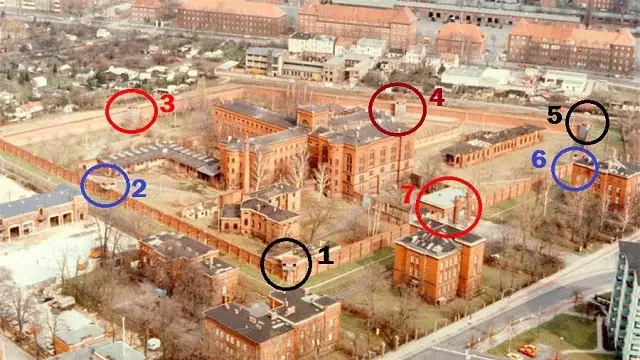 Aerial view of a large brick building complex with numbered sections in circles. Surrounded by trees and streets, urban background visible.