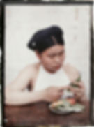 A person in a white top folds green leaves at a table with a plate of fruit. The background is plain. Text reads "TONKIN A 7764" above.