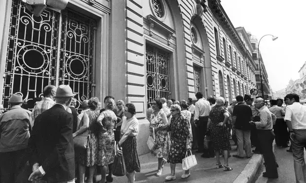 People in mid-century attire line up outside a historic building with ornate windows. The mood appears orderly and calm. Black and white image.