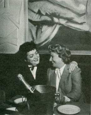 Two smiling women embracing, holding a champagne bottle, celebrating happily.