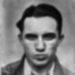 Black and white portrait of a young man with a serious expression. He wears a dark jacket and white shirt against a plain background.