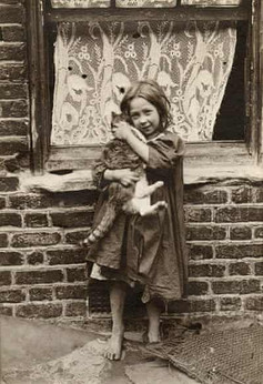 Young girl lovingly holds a cat by a brick wall and window.