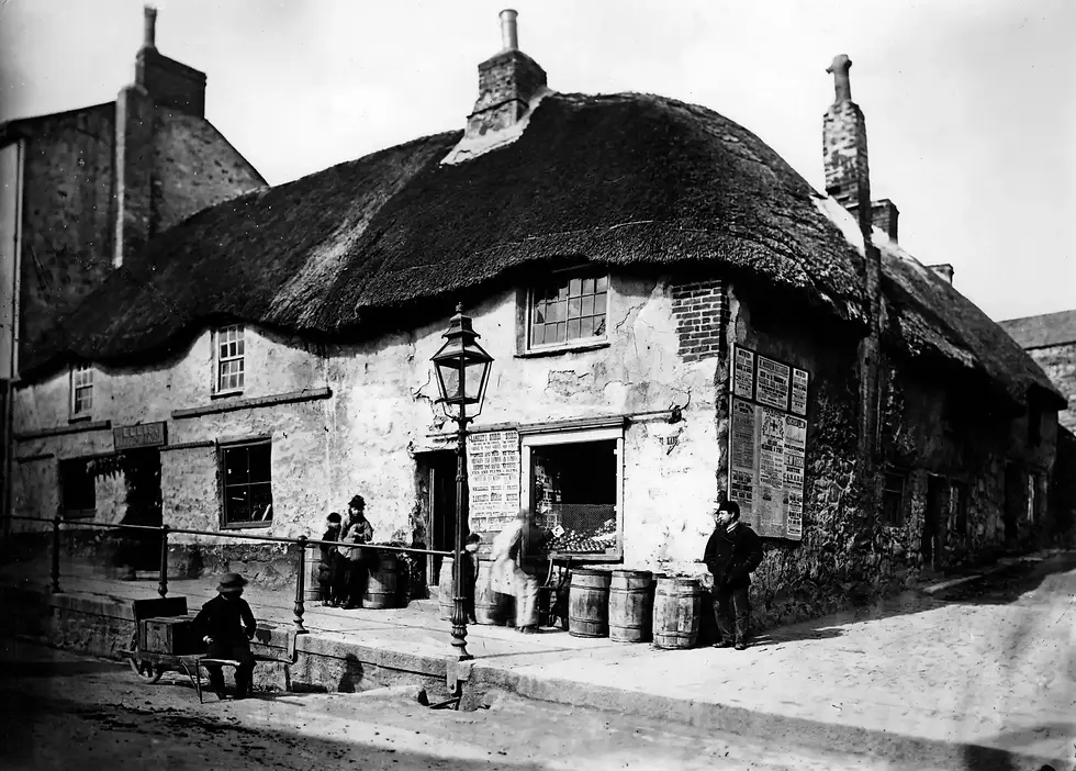 Historic black-and-white photo of a thatched-roof pub with people outside, including a seated man and children near barrels. Posters cover walls.