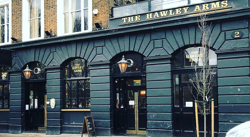 Brick pub facade with sign "The Hawley Arms." Street view, bike in foreground, clear sky, casual atmosphere. No people present.