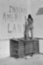 Activist painting "INDIAN AMERICA LAND" on wall, standing on wooden crate.