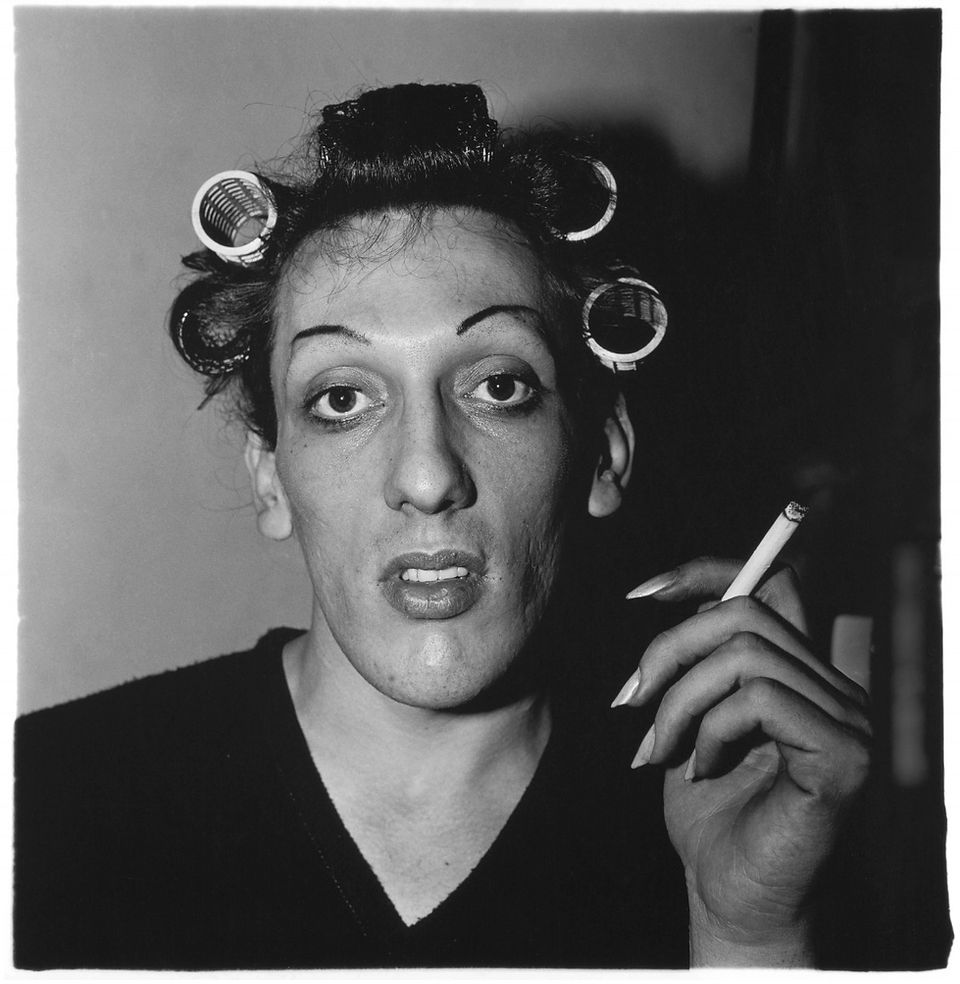 Glamorous person in hair curlers, dramatic makeup, holding cigarette.
