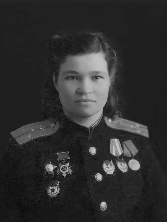 Woman in military uniform with shoulder insignia and multiple medals, posing against a dark background, conveying a sense of pride.