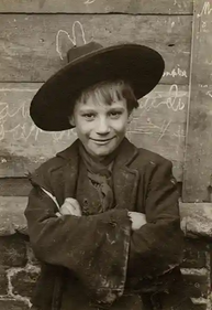 Young boy in wide-brimmed hat, smiling, arms crossed, historical attire.