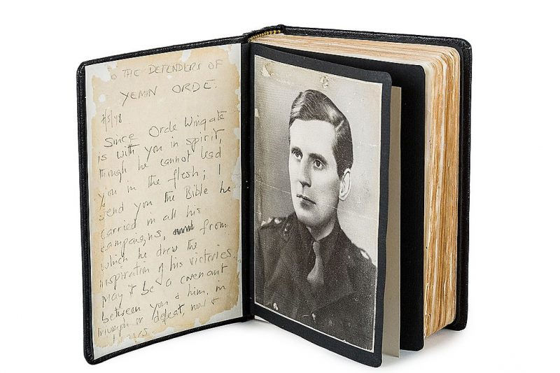 Open book displaying a black-and-white photo of a man in uniform and handwritten text on the left page. Pages are worn and yellowed.