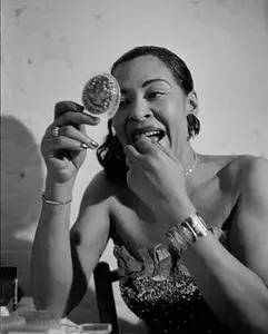 Billie Holiday looking intensely into a compact mirror, touching her lip.