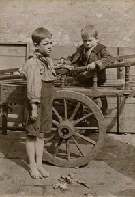 Two young boys, one standing, one sitting on an old wooden cart.