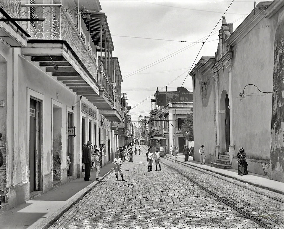 Cobblestone street with people, old buildings, and tram tracks in city.