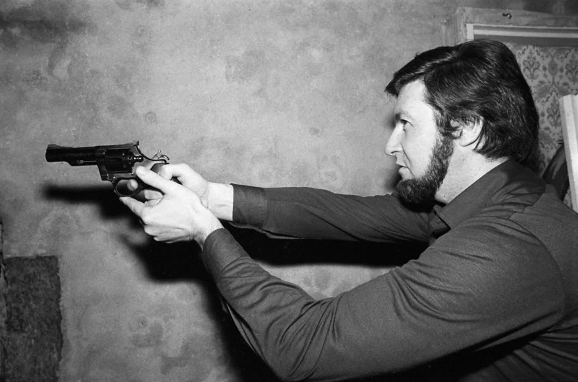 Side profile of a man with a beard aiming a gun