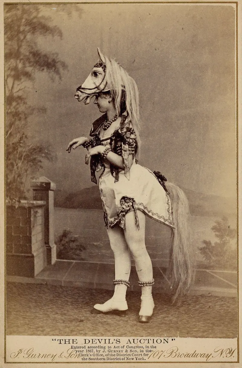 Woman wearing horse-head headdress, short costume with attached horsetail, rows of round beads or bells around ankles, wrists, neck and upper arm.