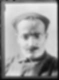 Portrait of a man wearing glasses and a cap, with a mustache. The image has a soft, blurred background, conveying a serious mood.