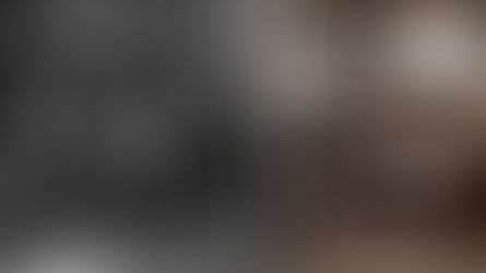 Historic market scene with men in hats carrying baskets and inspecting goods. Crowds gather around a vendor's table. Cobblestone street backdrop.