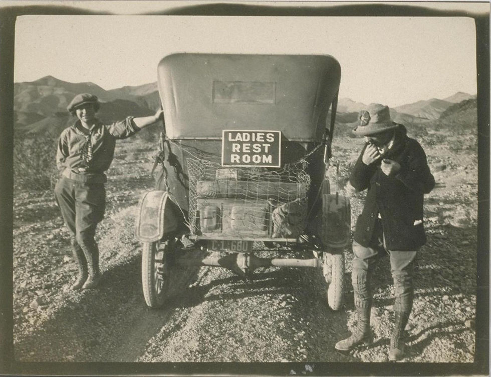 Two people, vintage car with "LADIES REST ROOM" sign, desert trip.