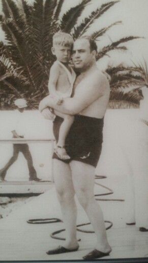 Vintage photo of man in swim trunks holding young child at beach.