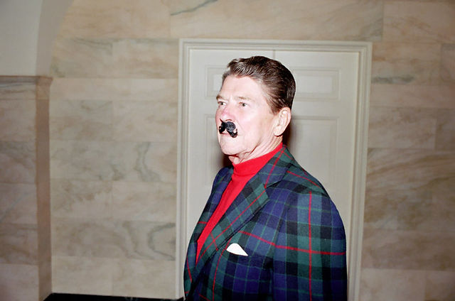 Ronald Reagan wearing red turtleneck, plaid jacket, Hitler-style mustache.