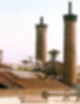 Helicopter on a rooftop near tall chimneys, with a person holding on to the building edge. Urban setting, clear sky, with industrial vibes.