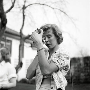 Young woman holding vintage camera to her eye, taking photo outdoors.