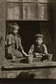 Two young children with solemn expressions gaze from a window.