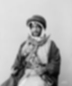Man in traditional attire with striped clothing and ornate headscarf, holding a decorative dagger. Neutral background with text "American Colony, Jerusalem."