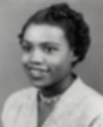 Smiling woman in vintage black-and-white photo, wearing a light-colored blouse and ornate necklace. Hair styled neatly. Elegant and positive mood.