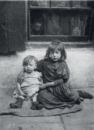 Black and white photo: two somber children sitting, face peers from window.