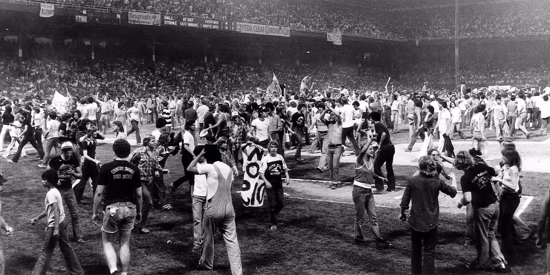 Crowds of fans filling the field at Comiskey Park after the disco records were blown up, one waving a Disco Sucks banner