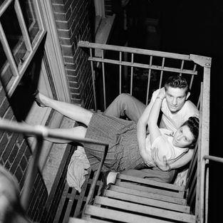 Young couple embracing intimately on a metal fire escape at night.